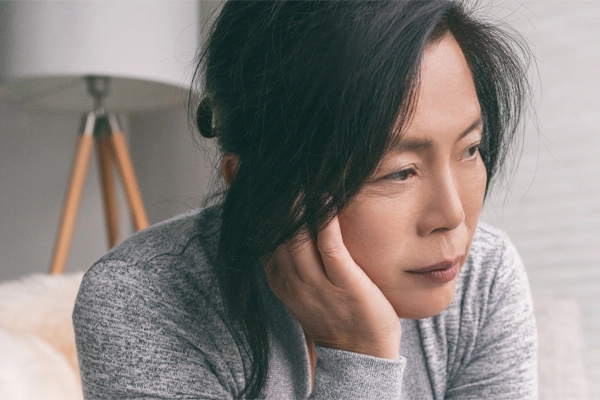 Adrenal-Fatigue-Doctor A middle-aged asian woman sitting on her couch, resting her head on her hand, suffering from adrenal fatigue. Get treatment for adrenal fatigue syndrome from Kane Lai, MD in Dallas-Fort Worth Metroplex.