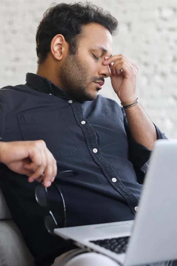Adrenal-Fatigue-Treatment A middle-aged man with a laptop closing his eyes and rubbing his nose. He needs treatment for Adrenal Fatigue Syndrome from Kane Lai, MD in Dallas-Fort Worth Metroplex.