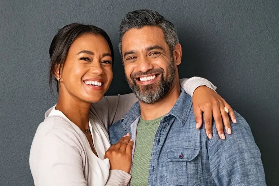Bioidentical-Hormone-Therapy-Doctor A middle-aged couple with their arms around each other standing against a gray background and smiling, happy with the bioidentical hormone therapy they received from Kane Lai, MD in Dallas-Fort Worth Metroplex.