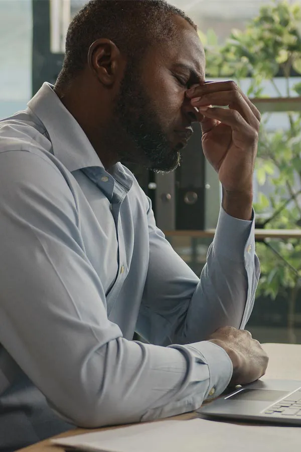 Chronic-Fatigue-Treatment A black man rubbing the top of his nose at his desk, in need of chronic fatigue treatment from Kane Lai, MD in Dallas-Fort Worth Metroplex.