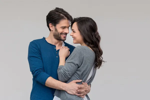 Erectile-Dysfunction-Doctor A man in a blue shirt embracing a woman in a gray shirt smiles due to his successful erectile dysfunction care from Kane Lai, MD in Dallas-Fort Worth Metroplex.