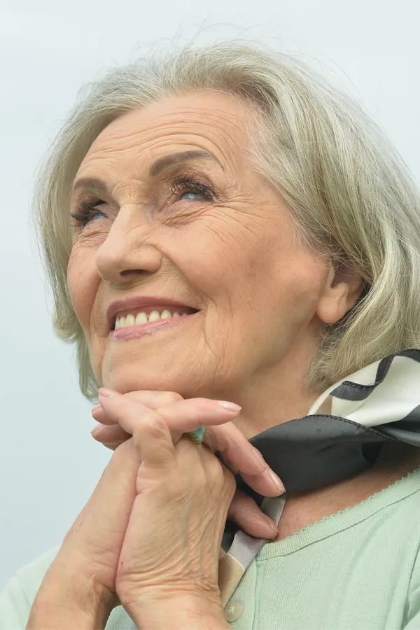 Hot-Flashes-and-Night-Sweats-Treatments An older woman holds her hands together under her chin and looks up at a cool sky smiling. Get treatment for hot flashes and night sweats from Kane Lai, MD in Dallas-Fort Worth Metroplex.