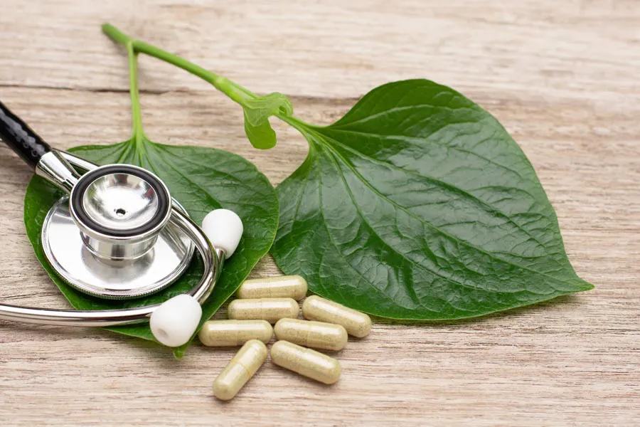 Integrative-Medicine-Clinic A stethoscope, leaves, and medicine capsules on a wood table, representing Integrative Medicine provided by Kane Lai, MD in Dallas-Fort Worth Metroplex.