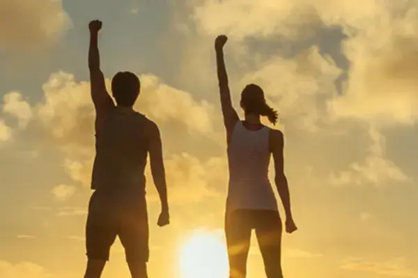 Ipamorelin-Peptide-Clinic A couple raise their right arms in the air in triumph, framed by the sunrise. Get Ipamorelin peptide treatment from Kane Lai, MD in Dallas.