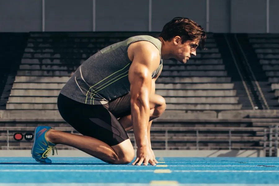 Lean-Muscle-and-Recovery-Clinic A white man kneels at the starting line on a track, determined to do his best. Get treatment for lean muscle loss and recovery from Kane Lai, MD in Dallas-Fort Worth Metroplex.