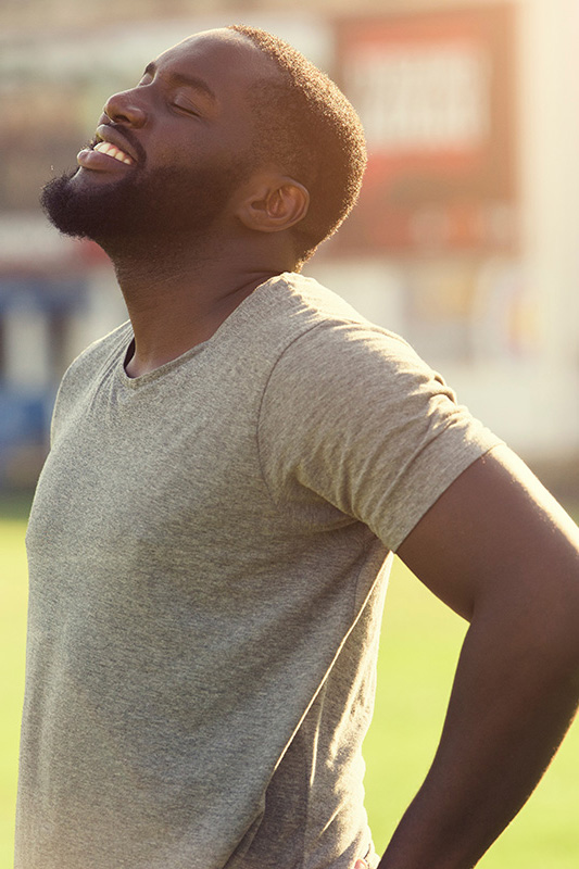Lean-Muscle-and-Recovery-Treatment A black man in a gray t-shirt and smiles, looking up with closed eyes after a satisfying workout. Get treatment for lean muscle loss and recovery from Kane Lai, MD in Dallas-Fort Worth Metroplex.