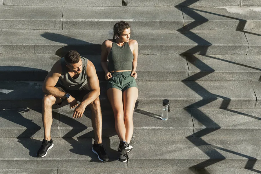 Medical-Weight-Loss-Doctor A couple in gray and green track clothes resting after a workout on stone steps, happy with their weight loss plans from Kane Lai, MD in Dallas-Fort Worth Metroplex.