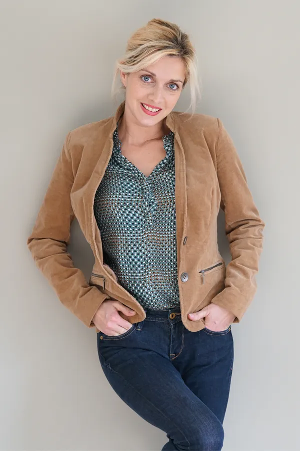 Metabolic-Syndrome-Treatment A smiling blonde woman in a tan leather jacket leans against a gray wall. Schedule metabolic syndrome from Kane Lai, MD in Dallas-Fort Worth Metroplex.