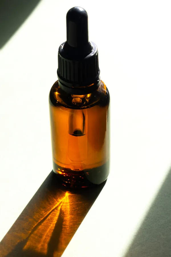 Performance-Enhancing-Peptides-Treatment A brown dropper bottle on a table lit by sunlight, representing performance enhancing peptide treatment from Kane Lai, MD in Dallas-Fort Worth Metroplex.