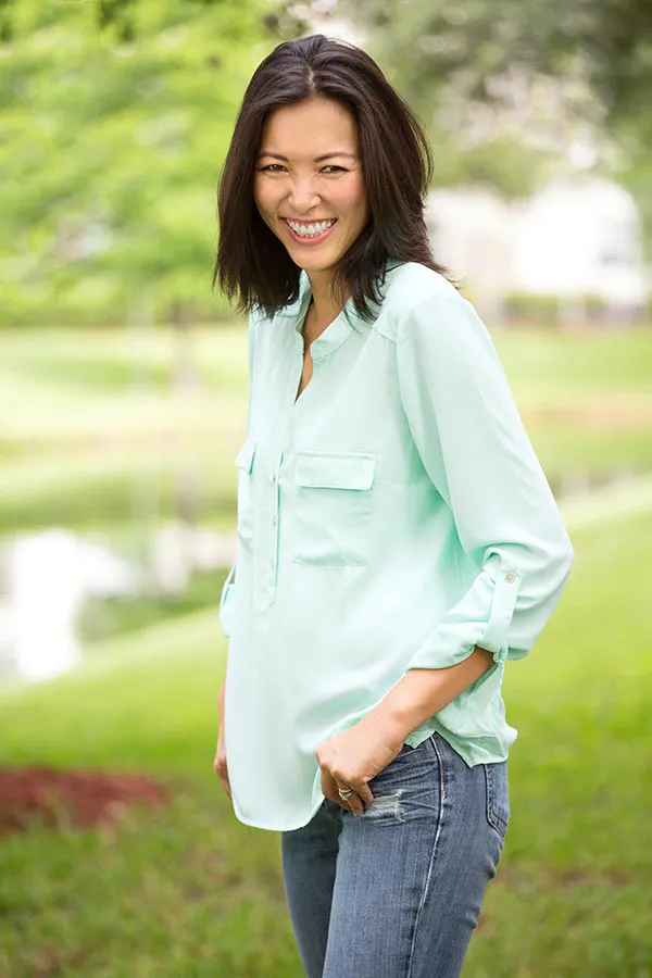 Perimenopause-Treatment A middle-aged brunette woman in a light green button-up shirt stands outside smiling, happy with her perimenopause treatment from Kane Lai, MD in Dallas-Fort Worth Metroplex.