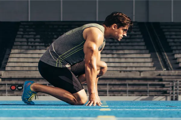Sermorelin-Clinic With a determined look, Aamuscular man in track clothes kneels at the start of a race. Get Sermorelin peptide therapy from Kane Lai, MD in Dallas-Fort Worth Metroplex.
