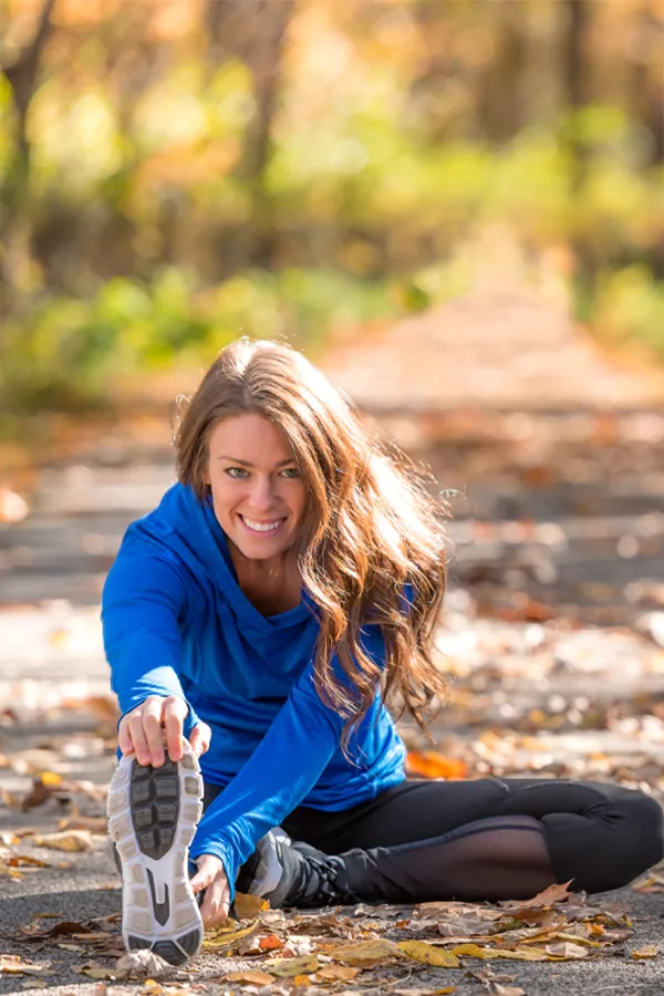 Sermorelin-Treatment A healthy woman in blue sweats stretches on a trail before a run. Get Sermorelin peptide therapy from Kane Lai, MD in Dallas-Fort Worth Metroplex.