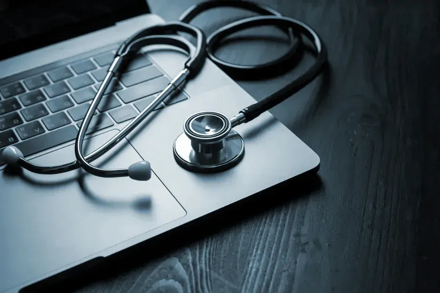Telemedicine-Doctor An open laptop with a stethoscope lying on it on a wooden table, symbolizing telemedicine care from Kane Lai, MD in Dallas.