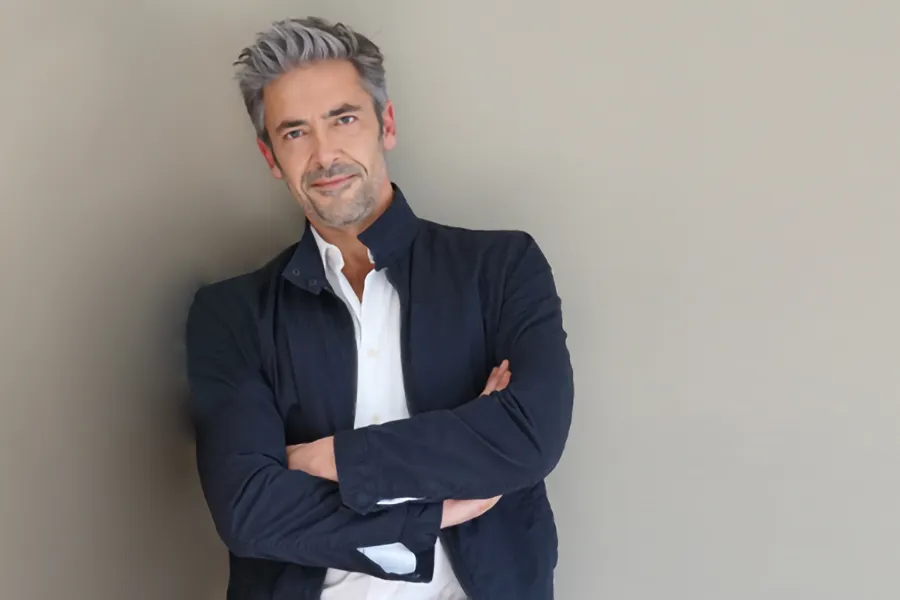 Testosterone-Low-T-Solutionsn-Clinic A middle-aged man in a white shirt and dark blue jacket leans against a gray wall smiling. Get testosterone for Low T from Kane Lai, MD in Dallas-Fort Worth Metroplex.