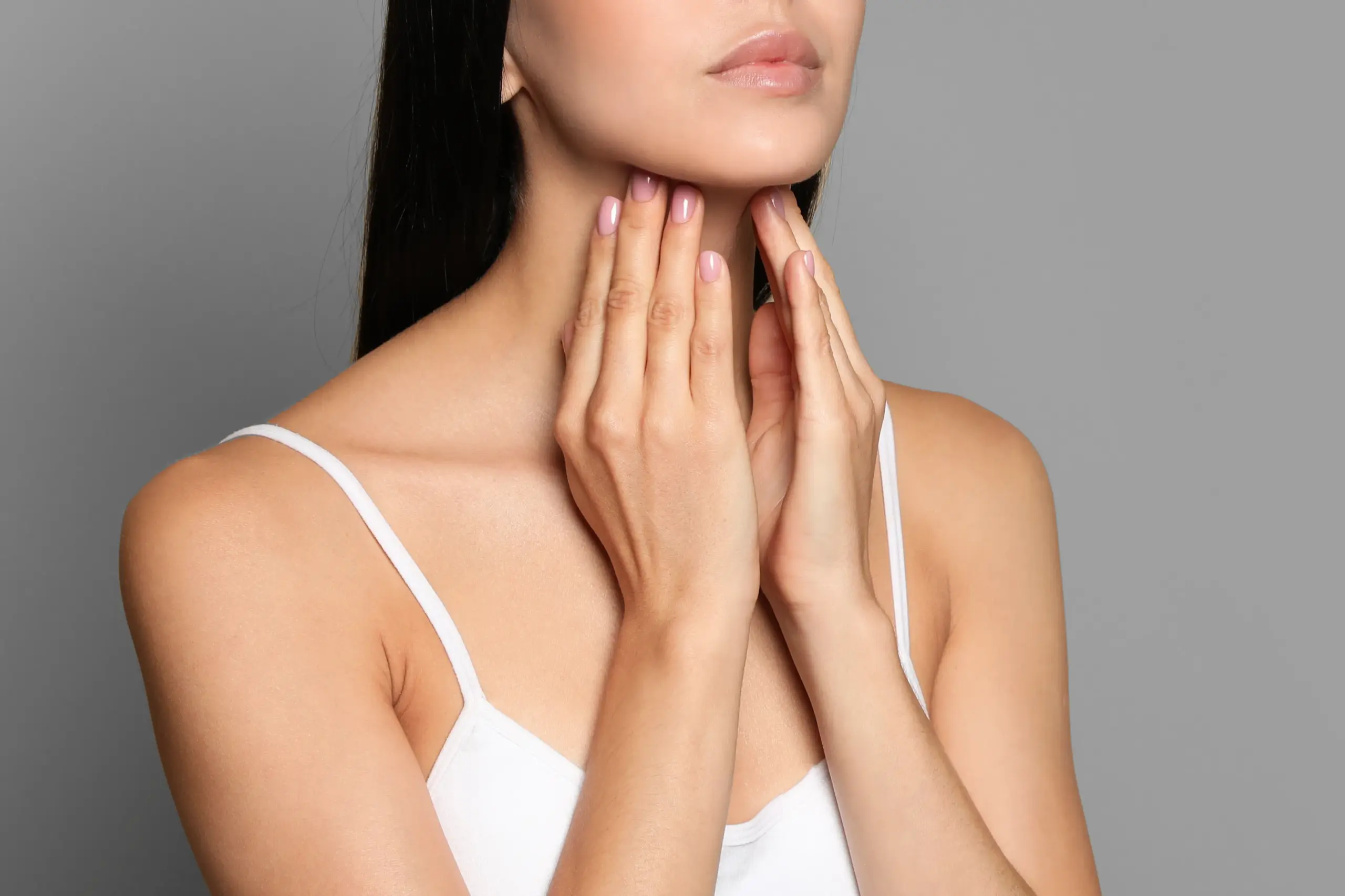 Thyroid-Doctor A woman in a white tank top touches her neck looking for signs of thyroid disorder. Get help for thyroid disorders from Kane Lai, MD in Dallas-Fort Worth Metroplex.