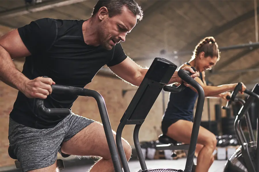 Tirzepatide-Doctor A couple in a brick gym work as hard as they can on exercise bikes, inspired by successful Tirzepatide treatment from Kane Lai, MD in Dallas-Fort Worth Metroplex.